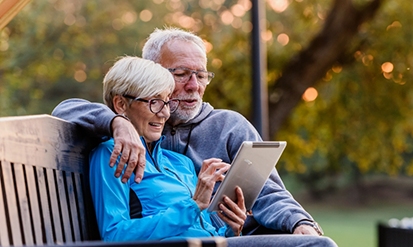 Senior couple sitting on a park bench and looking at a tablet