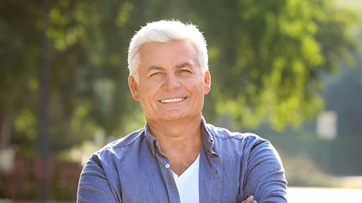 Older man in a blue collared shirt smiling outdoors