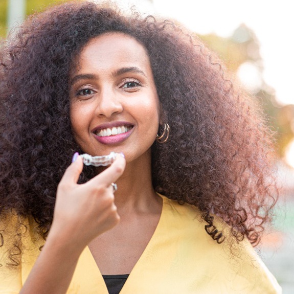 Woman with curly hair smiling while holding Invisalign