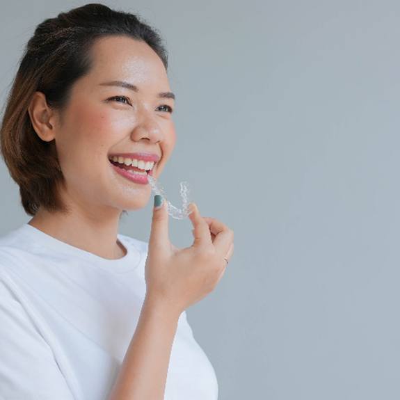 Woman in white shirt smiling while holding Invisalign