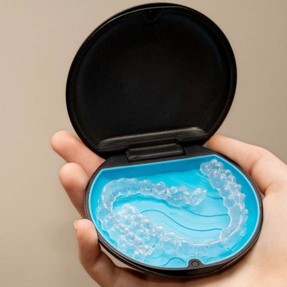 Patient holding up Invisalign aligners in black and blue case