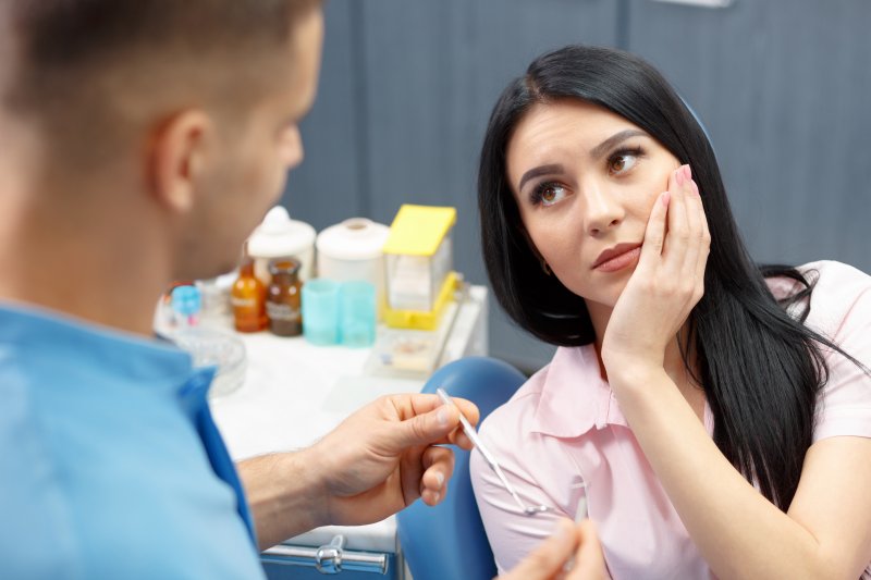 A woman holding her cheek at the dentist because she needs a root canal treatment